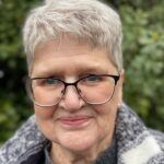 Senior woman wearing glasses with short silver hair smiling outdoors