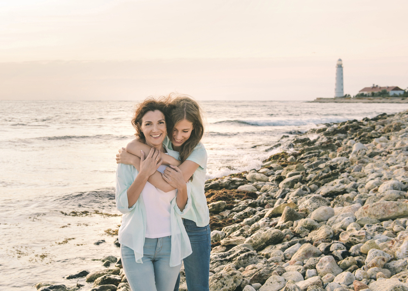 Mom and her teenage daughter hugging and smiling together over sunset sea view.Beautiful woman relaxing with her child.