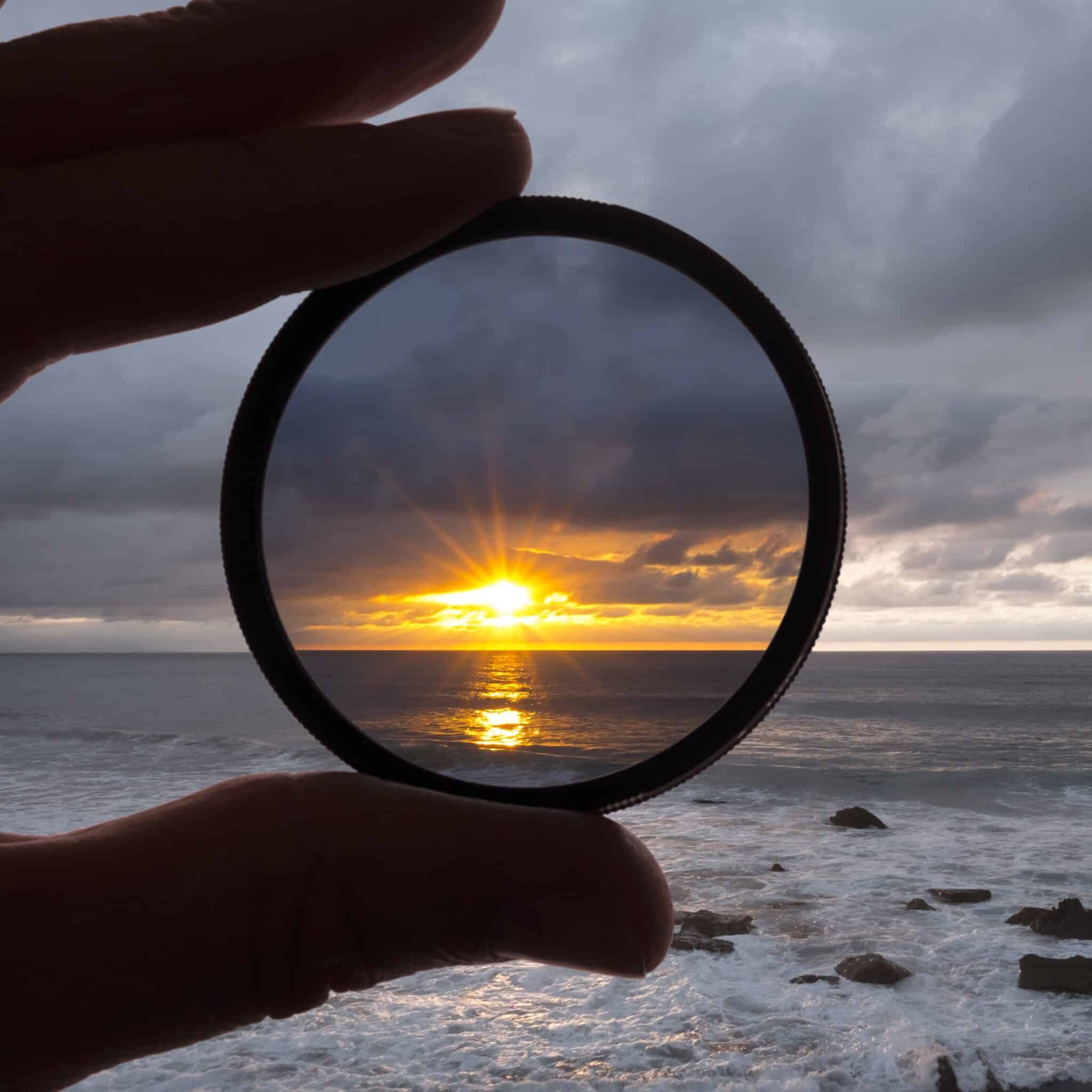 Black and White photo of the ocean with closeup of a hand holding a photo filter at sunset