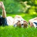 Three kids laying in green grass with their bare feet sticking up